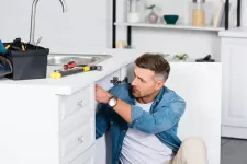 A toolbox sits on a counter as a person repairs a kitchen sink.