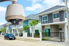 Close-up of a security camera with a suburban street lined with houses in the background.